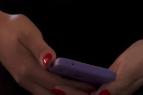 Imagem colorida de mão com unhas pintadas de vermelho segurando aparelho celular - Metrópoles