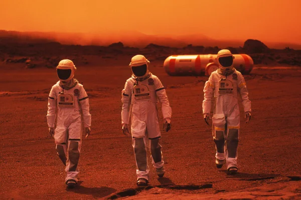 Imagem mostra três pessoas vestidas de astronauta em um cenário laranja, representando Marte - Metrópoles
