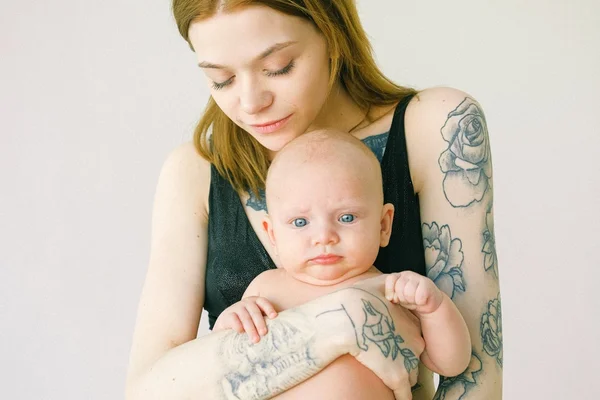 mãe com tatuagens segurando criança