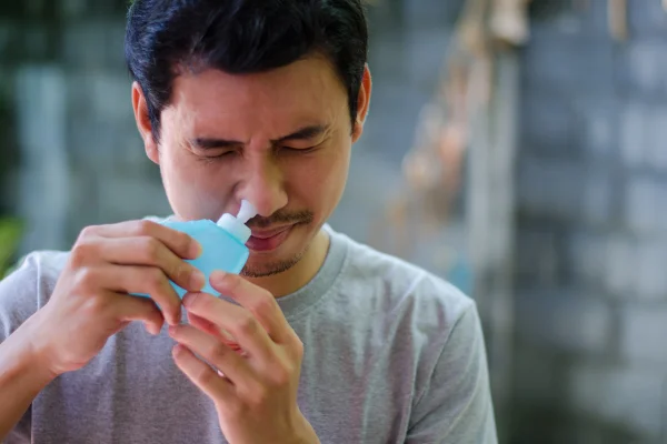 Imagem mostra homem de olhos fechados com um dispositivo azul encostado em uma das narinas - Metrópoles