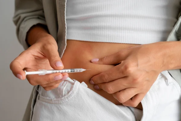 Foto colorida de mulher aplicando medicamento sob a pele da barriga - Metrópooles.