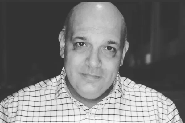 Imagem preto e branca mostra Zé Careca, homem branco, calvo, em imagem dos ombros para cima, vestindo camisa xadrez, em um fundo preto - Metrópoles