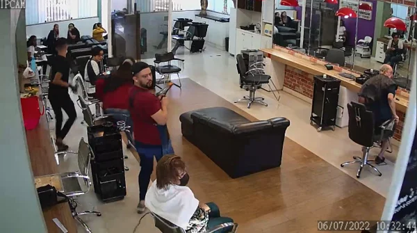 Homem de blusa vermelha reage a carro invadindo barbearia. Foto colorida
