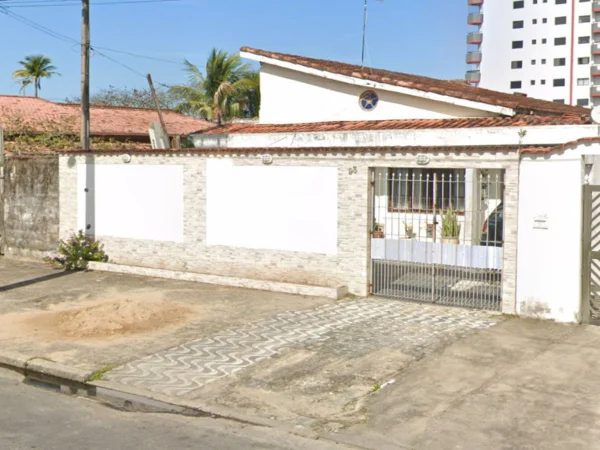 Foto colorida mostra fachada de casa com muro branco em dia de sol