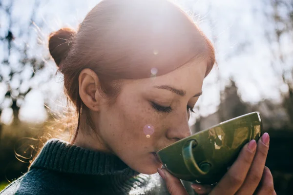 Foto colorida de mulher jovem tomando cháao ar livre em uma xícara ver - Metrópoles.