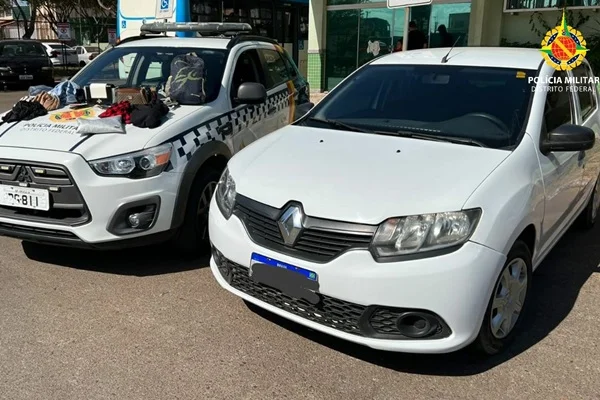 Fotografia colorida de viatura da polícia à esquerda e carro branco estacionado ao lado