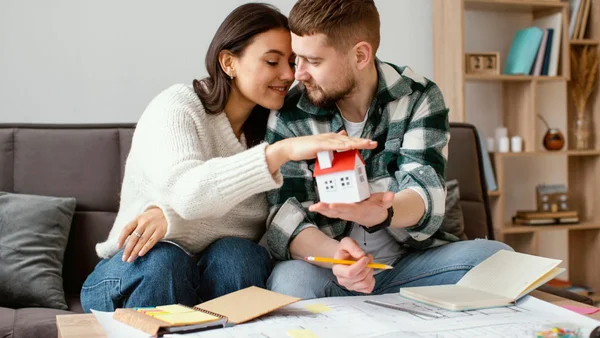 Casal segura casa em miniatura enquanto escreve planos futuros em caderno
