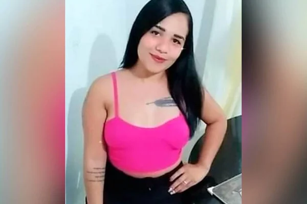 Mulher com blusa rosa e calça preta posa com mão esquerda na cintura e sorriso