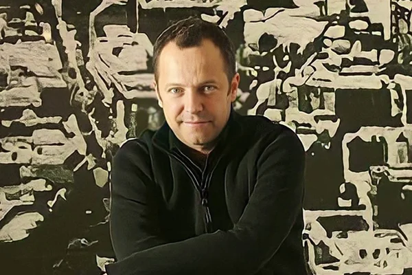 Foto do artista Vik Muniz. Ele usa casaco preto e está de braços cruzados - Metrópoles