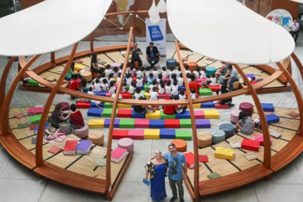 Foto de uma sala oval com almofadas, crianças sentadas e um casal na porta - Metrópoles