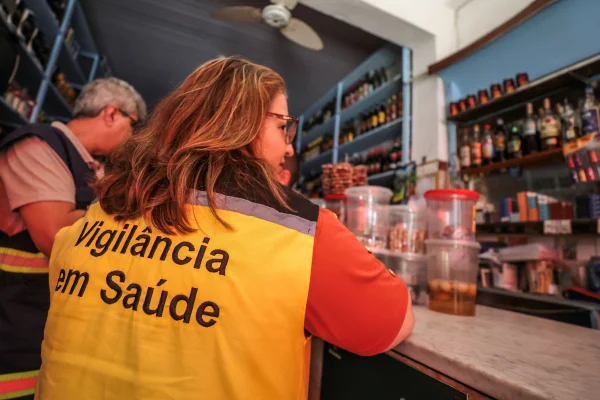 Imagem colorida de funcionária da Vigilância Sanitária de costas. Metrópoles