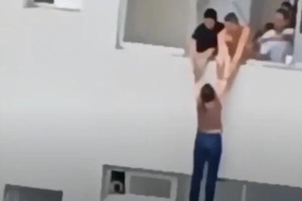 Mulher sendo resgatada por vizinhos depois de ficar pendurada quase cinco minutos em janela do 15º andar. -Metrópoles