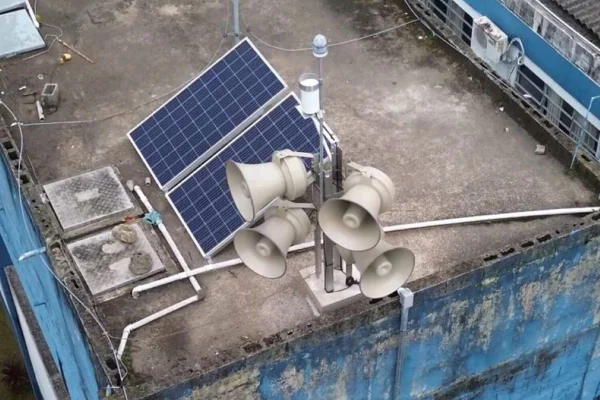 Imagens coloridas mostram sirenes no telhado de escola ao lado de painel azul que capta energia solar
