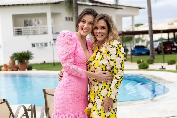Lara está do lado esquerdo usando um vestido rosa. Ela abraça SIlvana Chaves, que está usando um vestido amarelo com detalhes pretos - Metrópoles