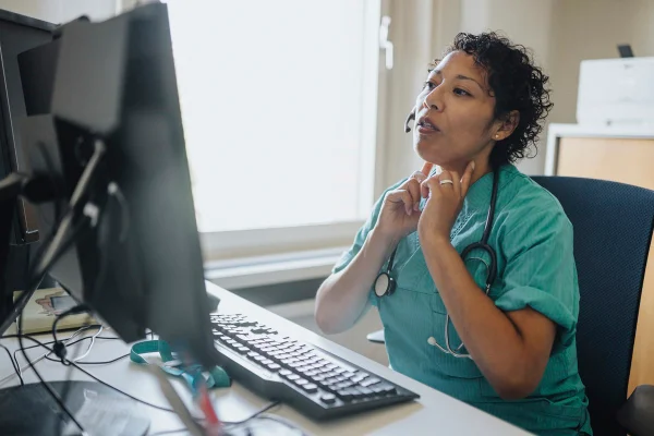 Jovem negra adulta em uma videochamada com paciente em casa. Conceito de telemedicina. Vista por cima do ombro. Teleconsulta. Telessaúde - Metrópoles