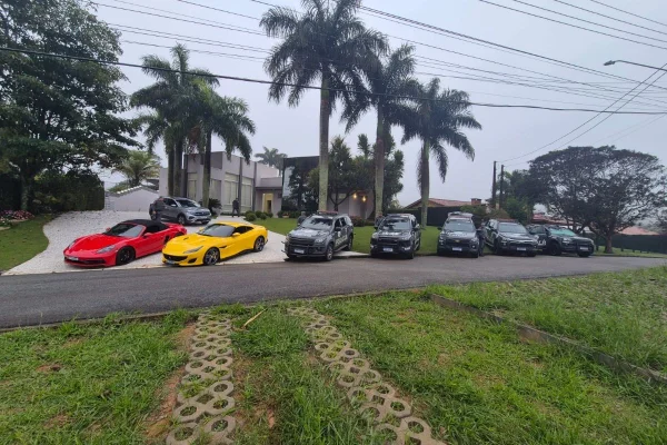 Foto colorida de carros de luxo e viaturas da Polícia Militar, em frente à casa de luxo de traficante em Itatiba, interior de São Paulo.