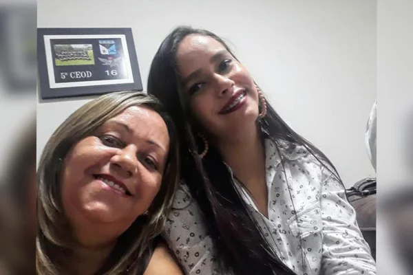 Foto coloridade mulher mais velha com a cabeça encostada no ombro de uma mulher mais nova, vestida com blusa branca e cabelos pretos longos. -Metrópoles