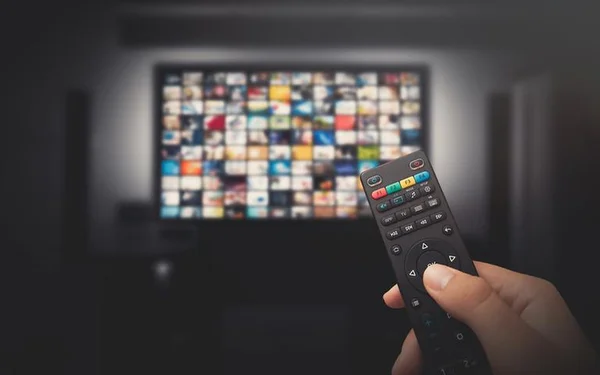 Mão segurando controle de TV em frente a uma tela