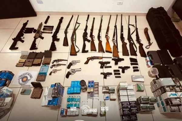 Imagens coloridas mostram espingardas, metralhadoras, pistolas e munições, dispostas no chão, todas frutos de apreensão e exibidas pela PM