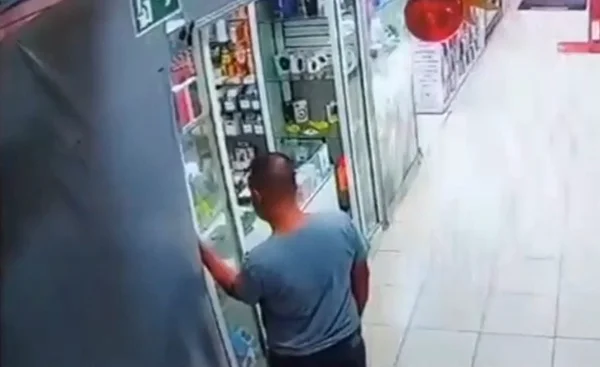 Imagem colorida mostra homem de camiseta azul furtando iPhone de dentro de uma vitrine de uma loja em uma galeria em Santos, no litoral de São Paulo - Metrópoles