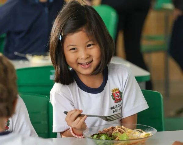 Fotografia colorida mostra menina comendo em escola-Metrópoles