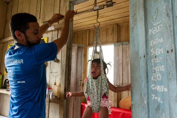 Foto colorida de médico pesando criança indígena no Amazonas - Metrópoles