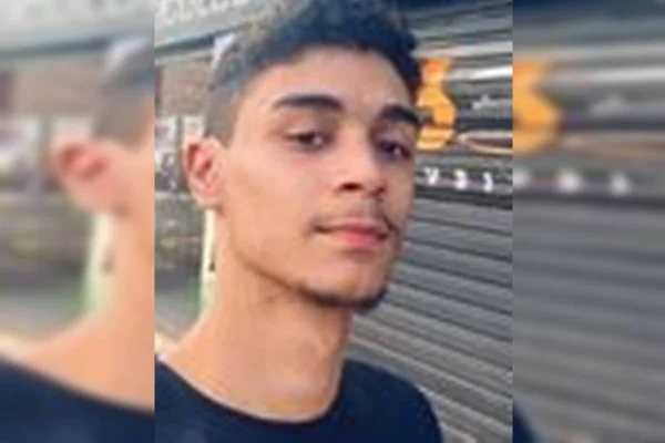 Imagem colorida de um jovem branco, de cabelos pretos curtos e cavanhaque. Ele veste camiseta preta