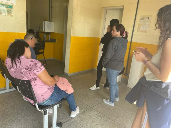 Foto colorida - pessoas sentadas e em pé aguardam atendimento no IML de Praia Grande