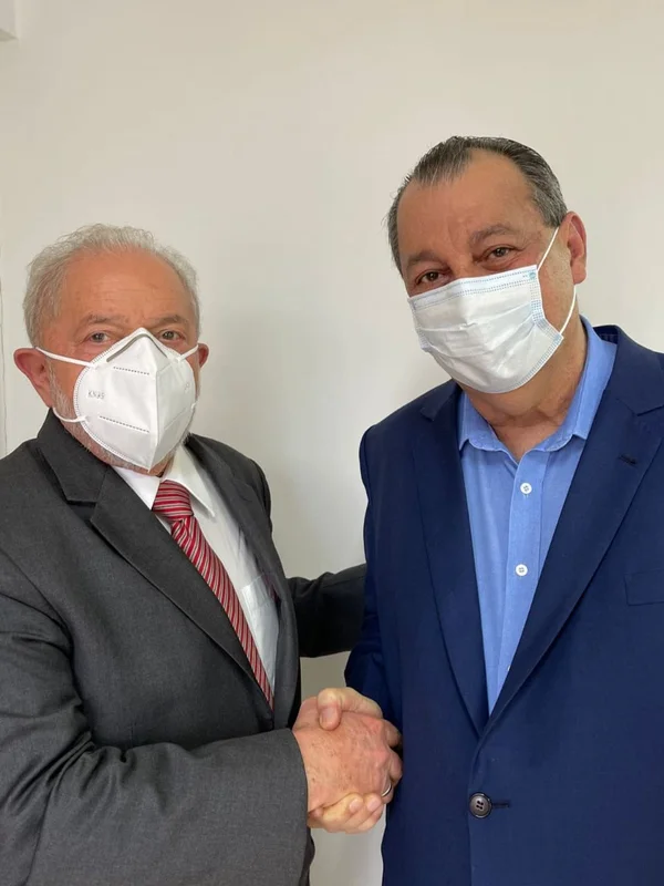 Ex-presidente Lula e senador Omar Aziz (PSD-AM) se encontraram em São Paulo. Eles dão as mãos, ambos de terno e de máscara, olhando para a câmera - Metrópoles