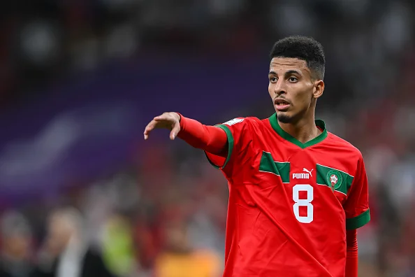 Jogar negro e de camisa vermelha da Seleção de Marrocos. Ele está parado e apontando para algo enquanto fala alguma coisa durante jogo de Marrocos na Copa do Mundo do Catar