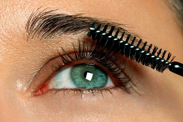 Mulher de olhos verdes penteando os cílios. Foto focada no olho