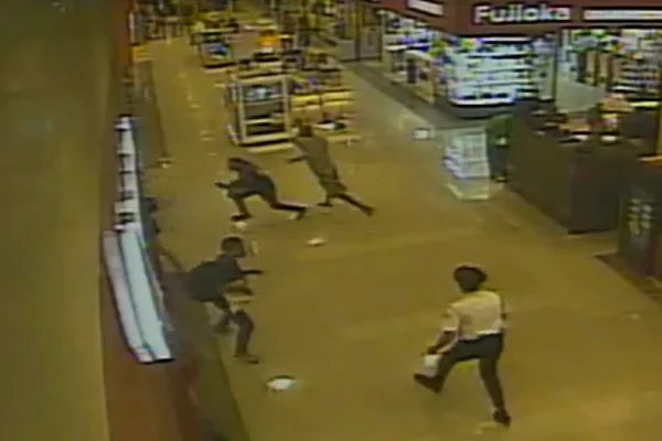 Imagem colorida, de câmeras de segurança, mostrando um homem atacando outro dentro de um shopping. Há seguranças de branco correndo atrás na cena, e ao redor, há lojas
