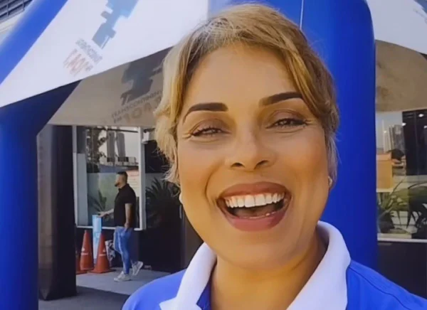 Foto colorida da locutora Eloise Matos, cabelo loiro com roupa e fundo azul - Metrópoles