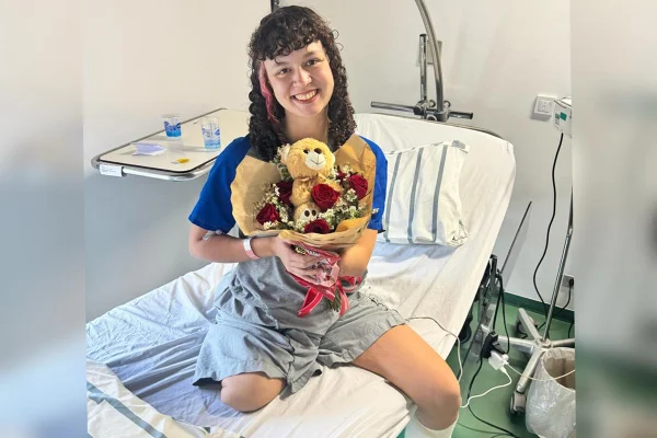 Foto colorida de menina em ambiente hospitalar segurando buquê de flores - Metrópoles.