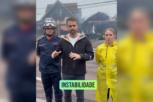 Imagem colorida de dois homens e uma pessoa em pé em frente a uma câmera - Metrópoles