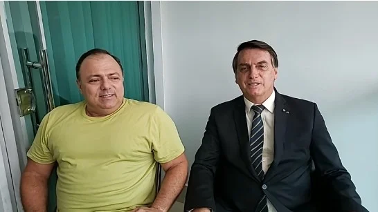 Presidente Jair Bolsonaro sentado ao lado de Eduardo Pazuello, em visita ao ministro da Saúde, com Covid-19