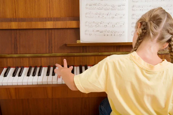 Foto de menina de costas tocando piano com partitura sobre instrumento musical - Metrópoles