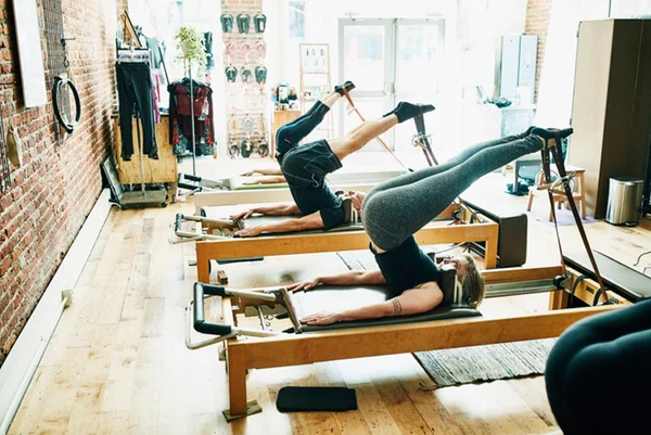Grupo de três pessoas praticando pilates em um estúdio - Metrópoles