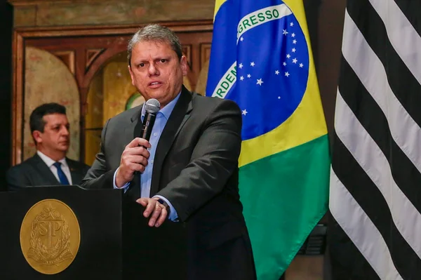 Fotografia colorida do governador Tarcísio de Freitas discursando em pé e segurando o microfone com a mão direita. Ao fundo, as bandeiras do Brasil e de São Paulo - Metrópoles