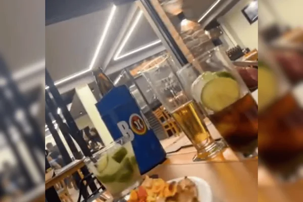 Imagem colorida de uma pizzaria, onde uma mulher branca vestida com uma roupa preta aparece armada com facão - Metrópoles