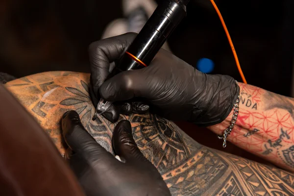 Foto colorida e com foco de uma pessoa sendo tatuaada, mostrando de perto a tinta que sai da máquina - Metrópoles.