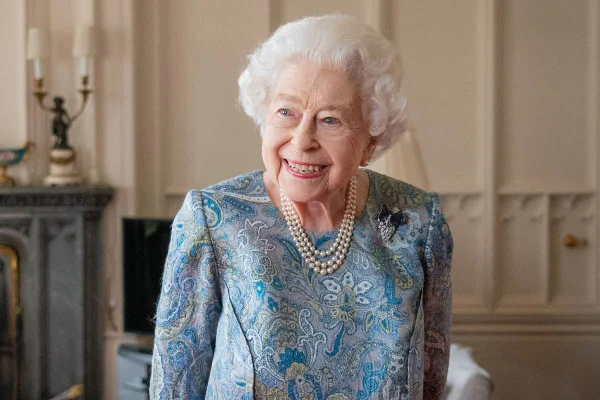 Foto colorida de mulher de cabelos brancos, colar de pérolas e vestido florido. Ela está sorridente - Metrópoles