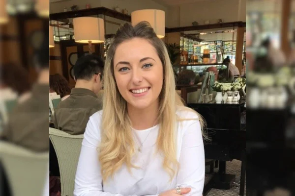 Imagem colorida de mulher de branco sentada em restaurante enquanto sorri para foto