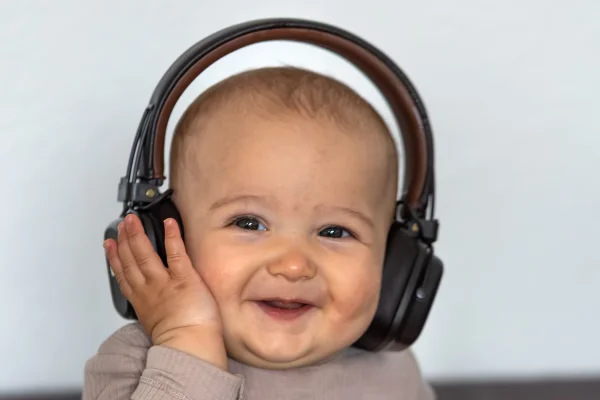 Foto colorida de bebê com fone de ouvido, ouvindo música e sorrindo para foto - Metrópoles.