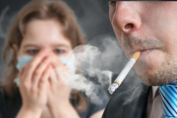 Foto colorida de homem fumando e mulher tampando o nariz - Fumante passivo: entenda como a exposição à fumaça prejudica o corpo - Metrópoles