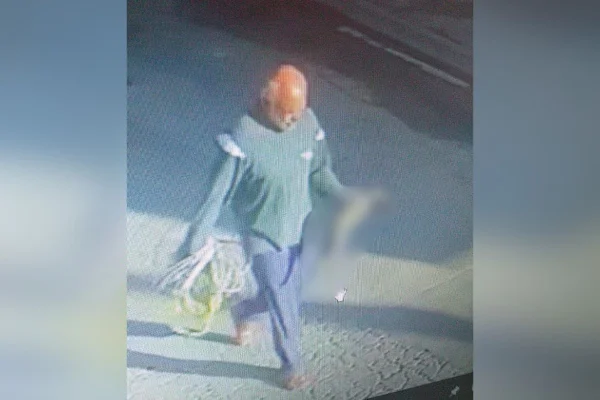 Imagem colorida mostra serial killer caminhando com gato morto. Metrópoles