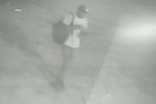 Homem com camisa branca, calça e mochila caminhando em imagem cinza