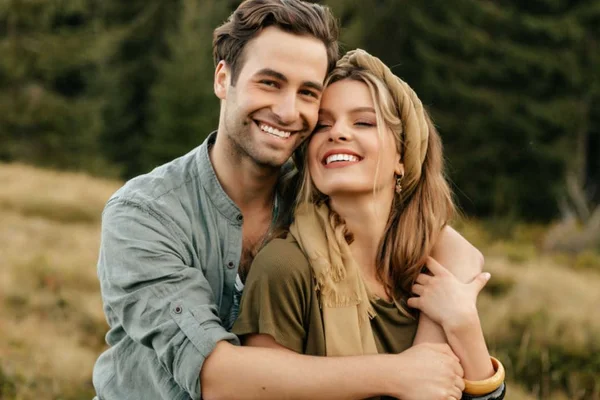 Casal se abraçando, mulher loira sorrindo com um homem sorrindo em uma paisagem verde - Metrópoles