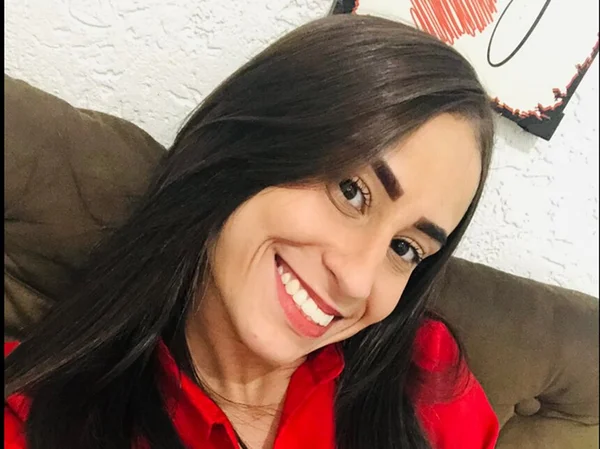Em foto colorida moça sorri usando camisa vermelha e com os cabelos negros soltos - Metrópoles