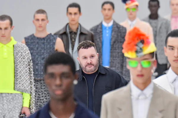 A imagem mostra o designer Kim Jones em meio à vários modelos com os rostos desfocados